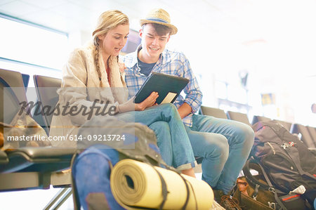 Young couple at airport, sitting, surrounded by backpacks, using digital tablet, low angle view