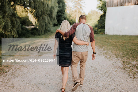 Romantic man and girlfriend strolling hand in hand on rural dirt track, rear view