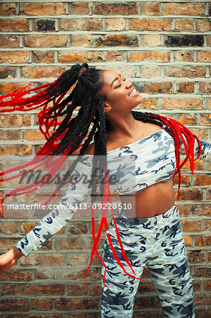 Carefree young woman in camouflage clothing dancing against brick wall