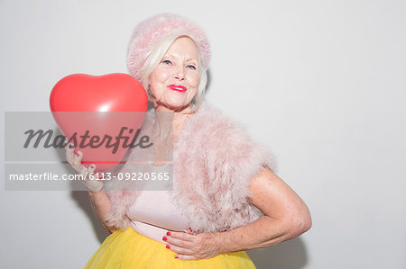 Portrait confident senior woman in fur holding heart-shape balloon