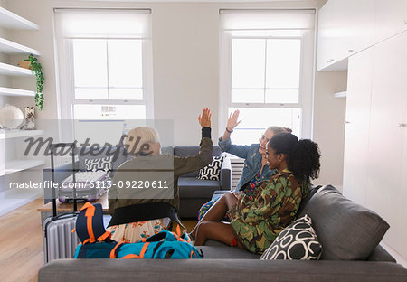 Young women friends with suitcases high-fiving in living room