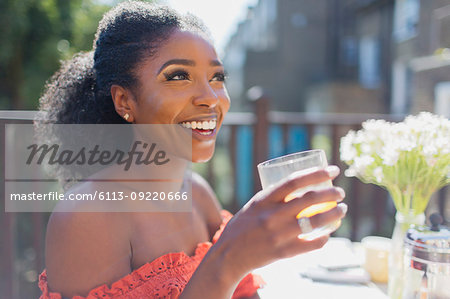 Happy young woman drinking orange juice on sunny balcony