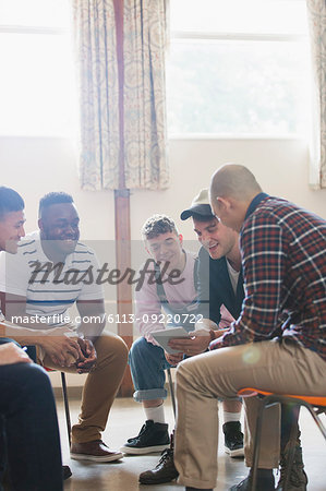 Men with digital tablet talking in group therapy circle
