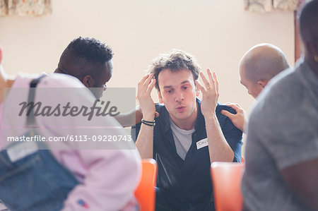 Men comforting man talking in group therapy