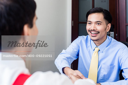Indonesian subordinate business professional talks to supervisor in office