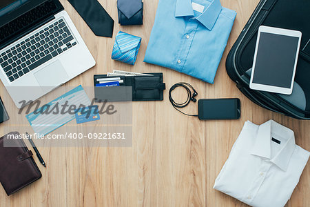 Businessman getting ready to leave for a business trip and packing a bag with formal clothing, accessories, laptop and plane tickets, traveling and business concept, flat lay