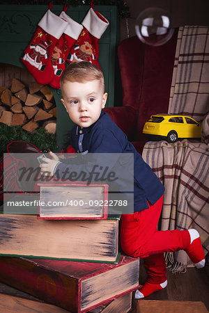 A boy in a dark blue sweater and red trousers at Merry Christmas decorated makes a wish for Santa Claus. Happy new year family concept with gift, plaid and fireplace