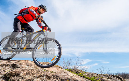 Cyclist in Red Jacket Riding the Mountain Bike Down Rocky Hill. Extreme Sport and Adventure Concept.