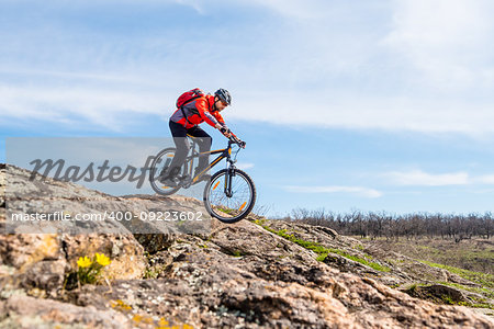 Cyclist in Red Jacket Riding the Mountain Bike Down Rocky Hill. Extreme Sport and Adventure Concept.