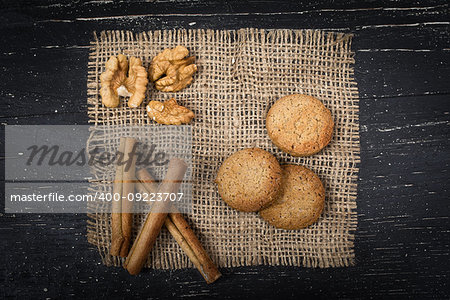 three oatmeal cookies, three cinnamon sticks and walnuts on burlap