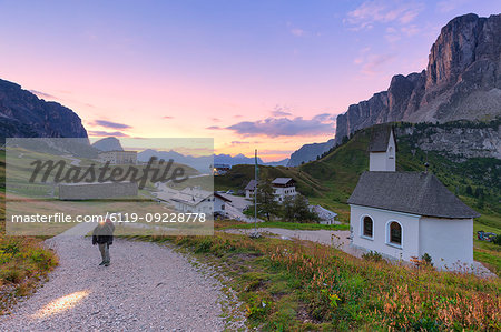 Hiker walks on a track during sunrise, Gardena Pass, Gardena Valley, South Tyrol, Dolomites, Italy, Europe