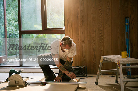 Construction worker measuring wood board in house