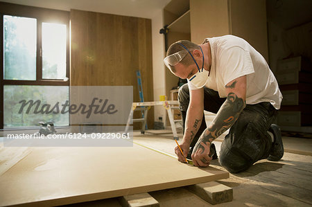 Construction worker with tattoos measuring and marking wood board in house
