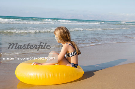 Girl sitting on yellow inflatable at beach, Castellammare del Golfo, Sicily, Italy