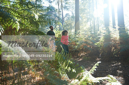 Female and male runners running together through sunlit forest ferns