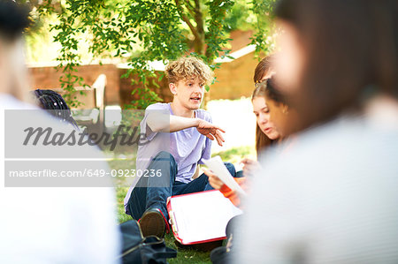 Male and female higher education students discussing paperwork on college campus lawn, over shoulder view