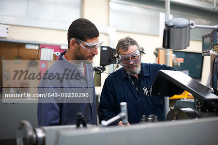 Lecturer teaching student to operate machine in workshop