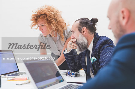 Businesswoman and men looking at laptop on office desk, over shoulder view