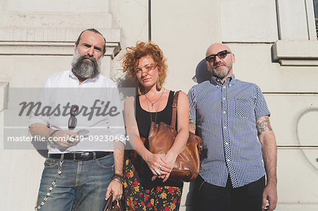 Mid adult woman and male friends leaning against wall in city, portrait