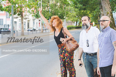 Mid adult woman and male friends hailing a cab on city street