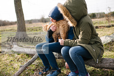 Brother and sister cuddling cat in field