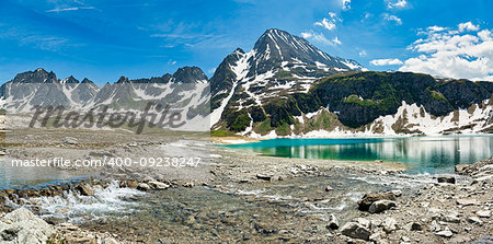 Lake Castel in Formazza Valley with river in foreground and mountains in backgroud wtih blue sky and clouds