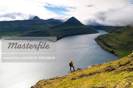Hiker on rocks looks at the fjords, Funningur, Eysturoy island, Faroe Islands, Denmark, Europe