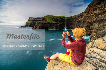 Man with smartphone snaps photos at Gasadalur waterfall, Vagar island, Faroe Islands, Denmark, Europe