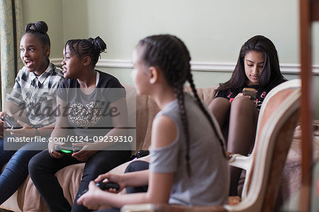 Tween girl friends playing video game on living room sofa