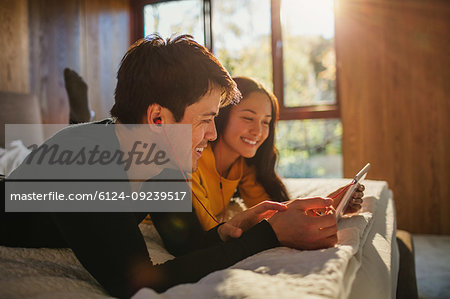 Happy couple with headphones sharing digital tablet on bed