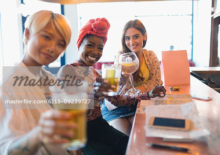 Portrait smiling, confident young women friends toasting cocktails in bar