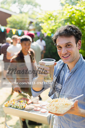 Portrait happy man drinking beer and barbecuing in backyard