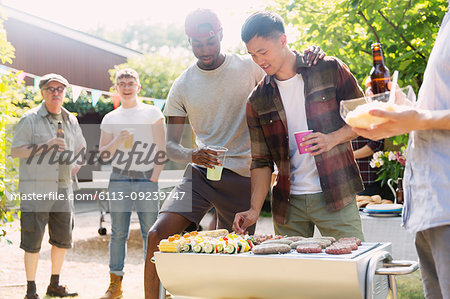 Male friends enjoying barbecue in sunny summer backyard
