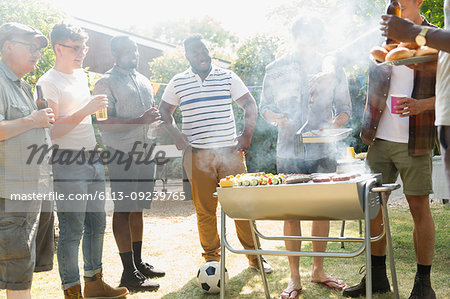 Male friends drinking beer and barbecuing in sunny summer backyard