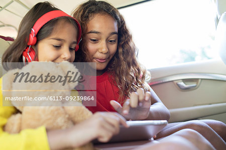 Sisters using digital tablet in back seat of car