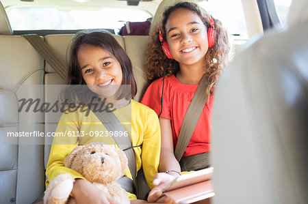 Portrait happy sisters with teddy bear riding in back seat of car