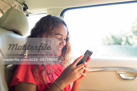 Smiling tween girl using smart phone in back seat of car