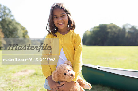 Portrait smiling, cute girl with teddy bear in sunny field