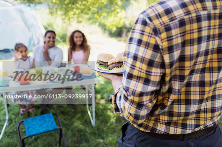 Father serving barbecue hamburgers to family at campsite table