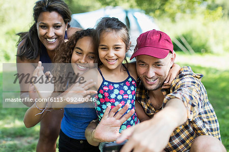 Happy family waving, taking selfie with camera phone at campsite