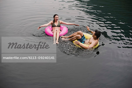 Young couple floating on lake in inflatable rings