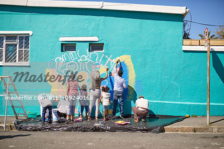 Community volunteers painting vibrant mural on sunny urban wall