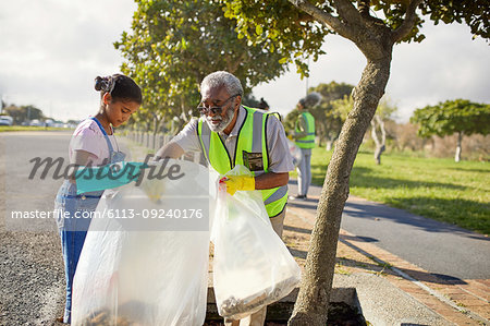 Grandfather and granddaughter volunteers cleaning up litter in sunny park