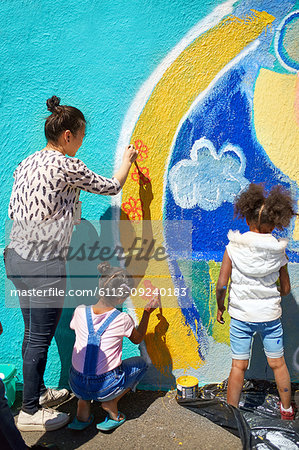Mother and daughter volunteers painting vibrant mural on sunny wall