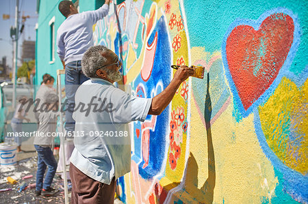 Senior man painting mural on sunny urban wall