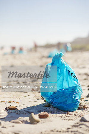 Blue cleanup garbage bag on sunny, sandy beach