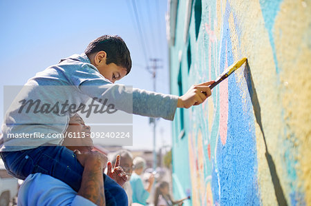 Father and son volunteers painting mural on sunny wall