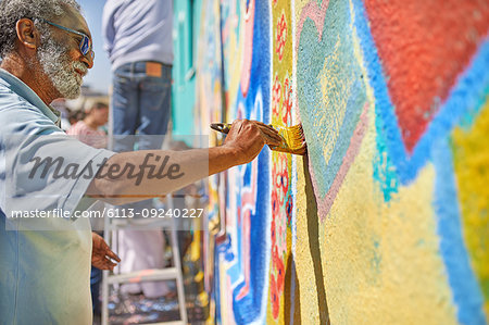 Senior man painting mural on sunny wall