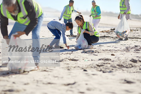 Mother and son volunteers cleaning up litter on sunny, sandy beach