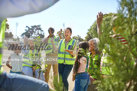 Enthusiastic volunteers cheering, planting trees at sunny park